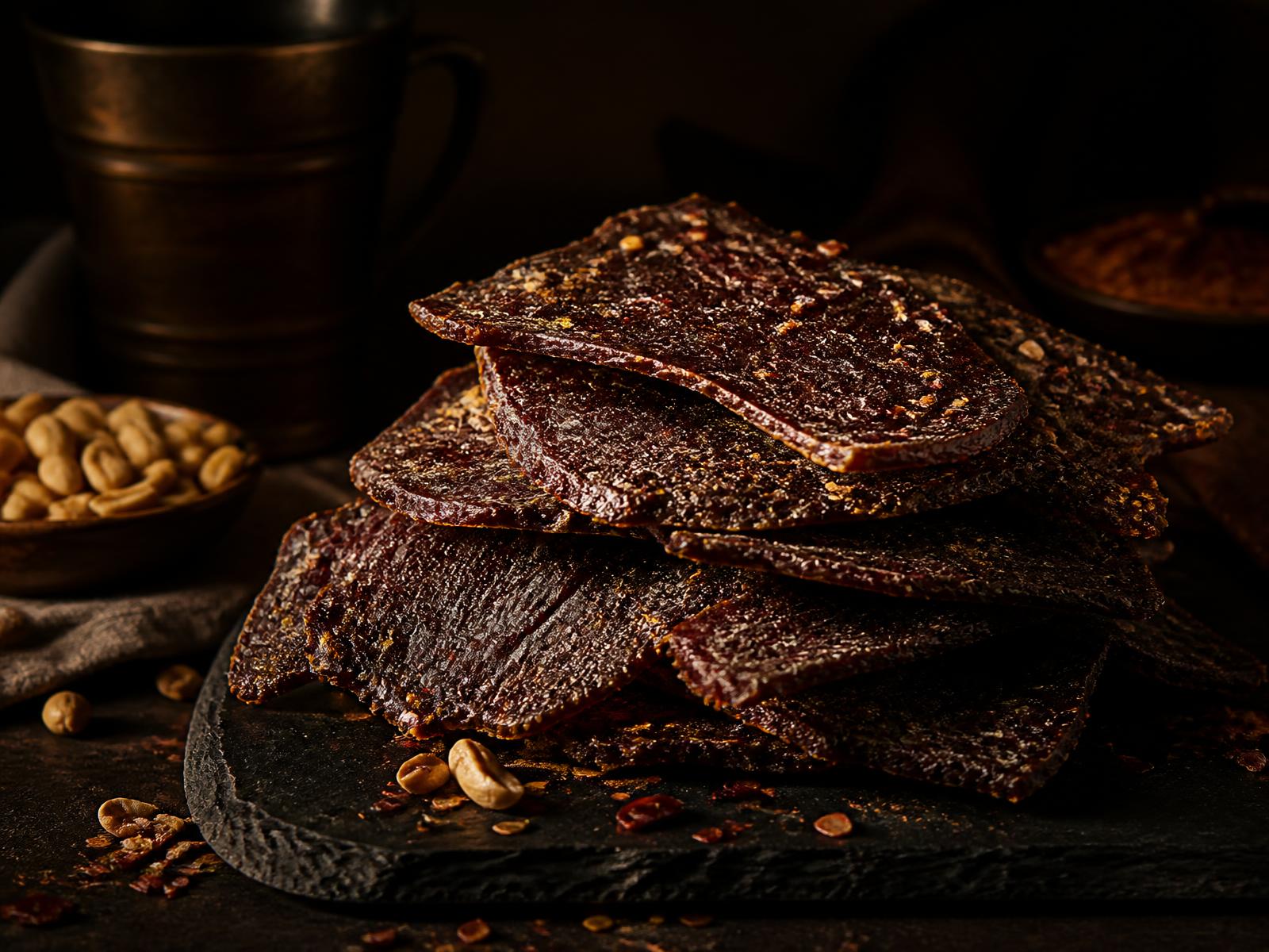Stacked slices of premium spiced kilishi beef jerky on a dark slate board